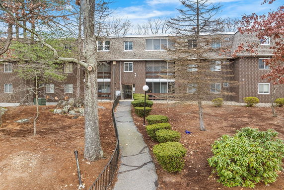 Front view of a multi-story brick apartment building with a pathway leading to the entrance.