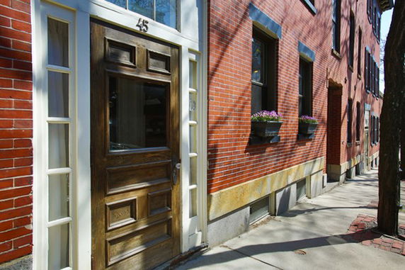 Front view of a brick townhouse with a wooden door and window flower boxes.
