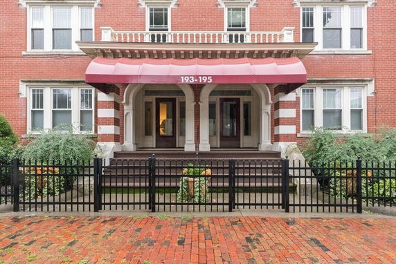 Front view of a multi-story brick building with an awning and a black fence.
