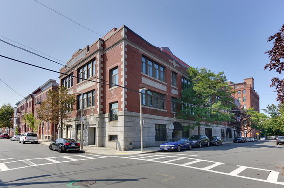 Front view of a large, multi-story brick building on a street corner.