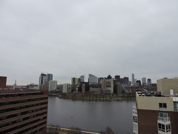 Panoramic view showing a river with city buildings in the background under a cloudy sky.