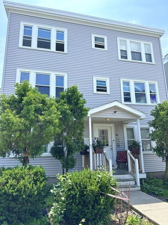 Front view of a three-story house with a small porch and multiple windows.