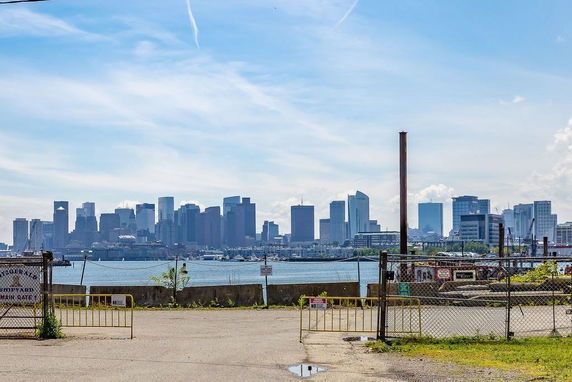 View of a city skyline with skyscrapers across a body of water seen from a fenced area.
