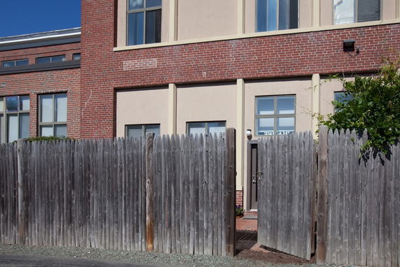 Front view of a building with brick and stucco facade, partially obscured by a wooden fence.