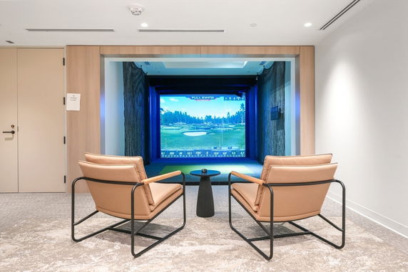 Indoor golf simulator room with chairs and a screen.