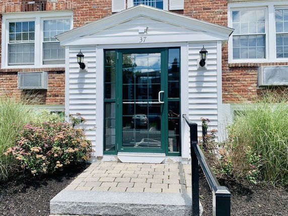 Front view of a brick building entrance with a glass door and white trim.