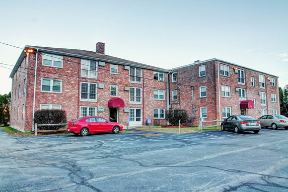 Front view of a multi-story brick apartment building with parking area.