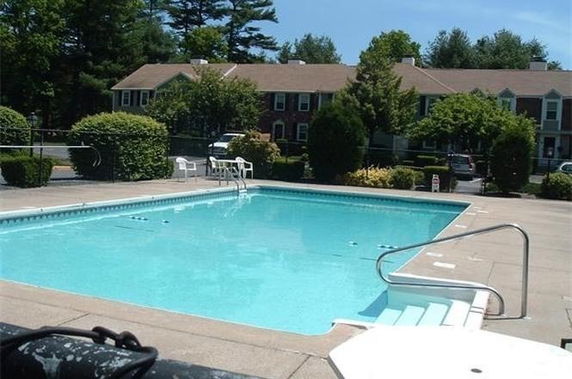 Swimming pool with surrounding patio area and residential townhouses in the background.