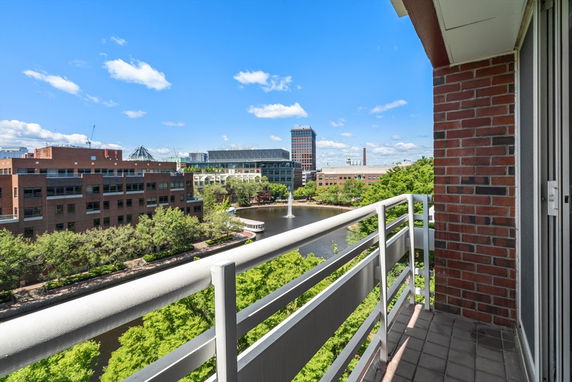 View from a balcony overlooking a river and surrounding cityscape with buildings and greenery.