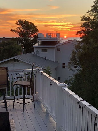Rooftop deck with chairs overlooking a sunset view of surrounding houses and trees.