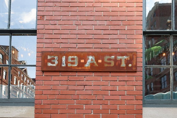 Front view of a brick building with large windows and a rusted metal address plaque.