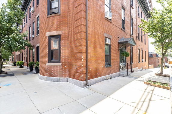 Corner view of a brick multi-story building with several windows and a small entrance canopy.