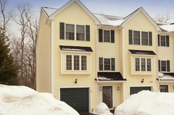 Front view of a yellow multi-story house with garage and snow-covered surroundings.