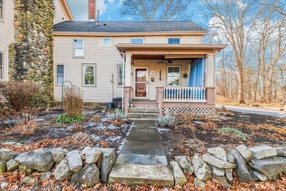 Front view of a two-story house with a porch and stone chimney.