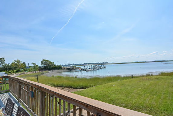 Panoramic view of a waterfront with grassy areas and a pier extending into the water.