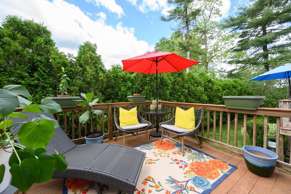 Deck area with chairs and umbrellas surrounded by greenery.
