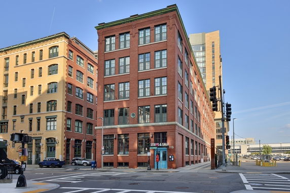 Front view of a multi-story brick building on a street corner with large windows.