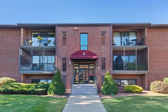 Front view of a brick residential building with balconies and a red awning above the entrance.