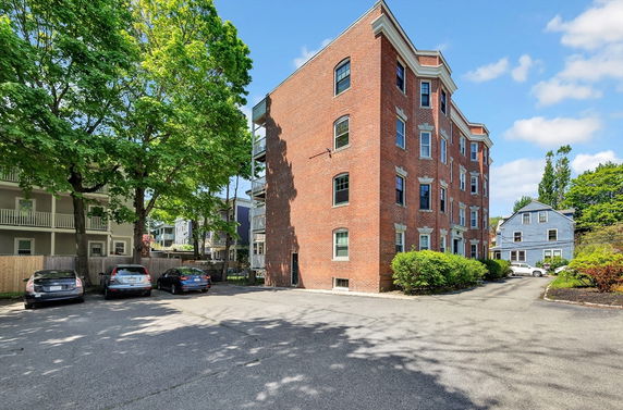 Front view of a brick multi-story building with a paved parking area.