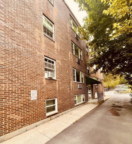 Side view of a brick apartment building with multiple windows and a small entrance canopy.