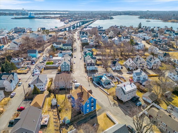 Aerial panoramic view of a residential neighborhood with houses and roads, overlooking a bridge and a body of water.