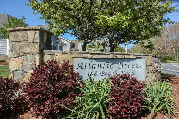 Front view of a sign for a building complex with stone pillars and greenery around it.