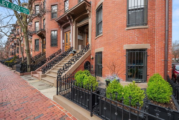 Front view of a brick townhouse with ornate iron railings and steps leading to the entrance.