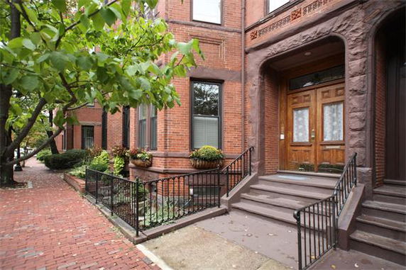 Front view of a brick residential building with wooden doors and steps.