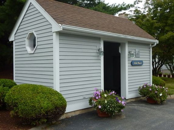 Front view of a small shed with light blue siding and a brown gable roof.
