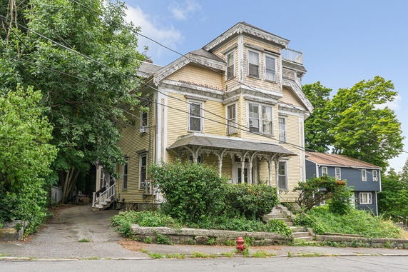 Front view of a large, multi-story house with ornate details and a yellow exterior.