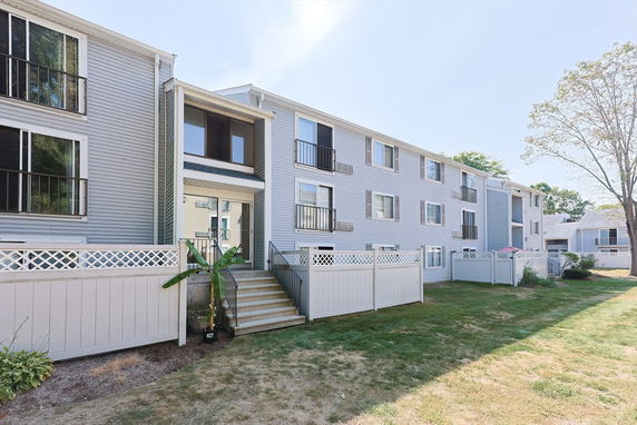 Front view of a multi-story apartment building with balconies and fenced entrance.