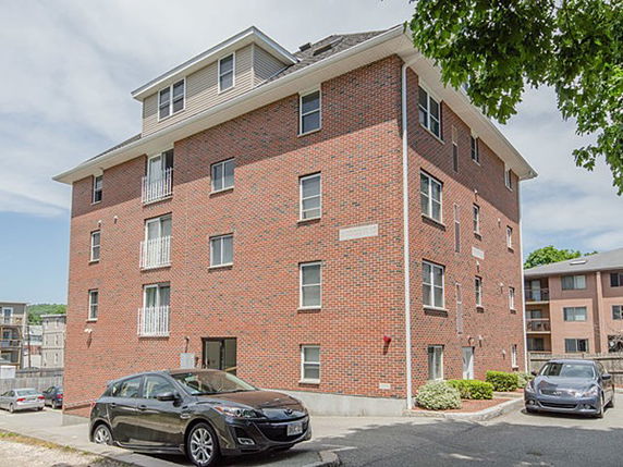 Front view of a multi-story brick building with several windows and a small parking area.
