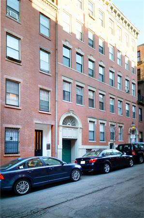 Front view of a multi-story brick building with parked cars in front.