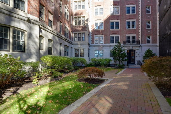 Front view of a multi-story brick building with multiple windows and a small garden in front.