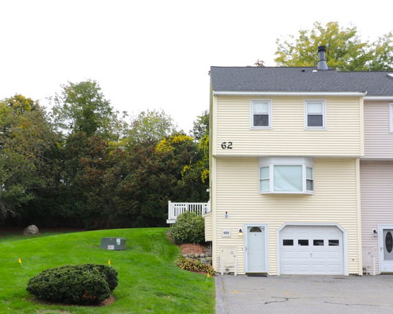 Front view of a beige two-story townhouse with attached garage and bay window.