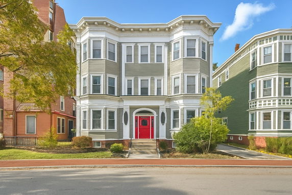 Front view of a three-story house with a red door and bay windows.