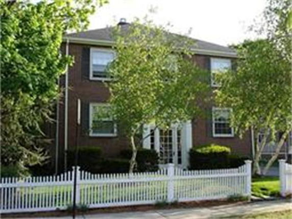 Front view of a two-story brick house with a white picket fence.