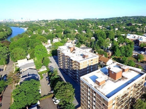 Aerial view of apartment buildings surrounded by greenery and a river nearby.