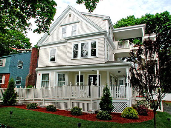 Front view of a multi-story white house with a porch and railing.