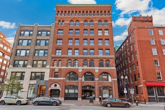 Front view of a multi-story brick building with arched windows and three entries.