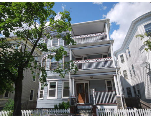 Front view of a multi-story residential building with balconies and a white picket fence.