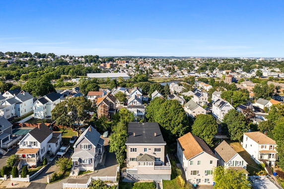 Aerial view of a suburban neighborhood with multiple houses, trees, and distant greenery.