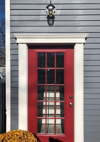 Front view of a house with a red door and grey siding.
