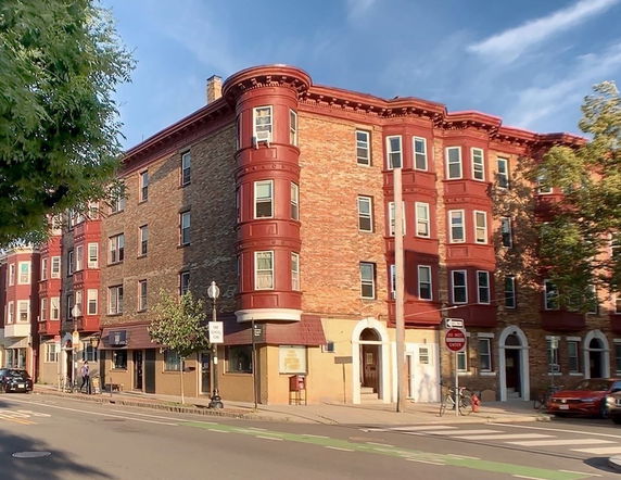 Front view of a multi-story brick building with red trim and multiple windows.