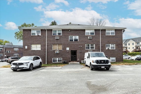 Front view of a three-story brick apartment building with parking area in front.