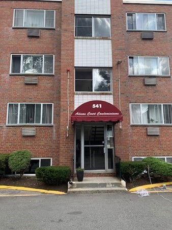 Front view of a multi-story brick condominium building with multiple windows and a red awning over the entrance.