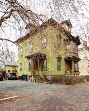 Front view of a green two-story house with dormer windows and a small front porch.