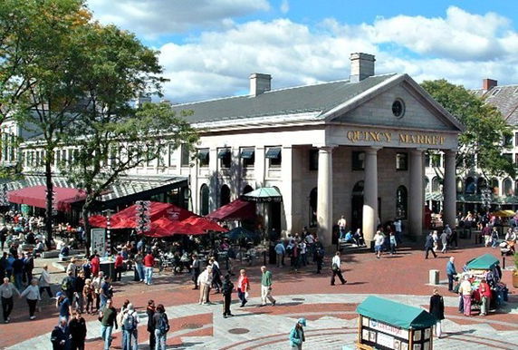 Front view of a building with columns and people gathered around.