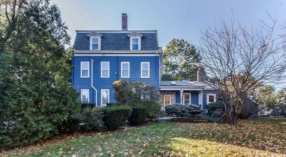 Front view of a multi-story blue house with dormer windows and a chimney.