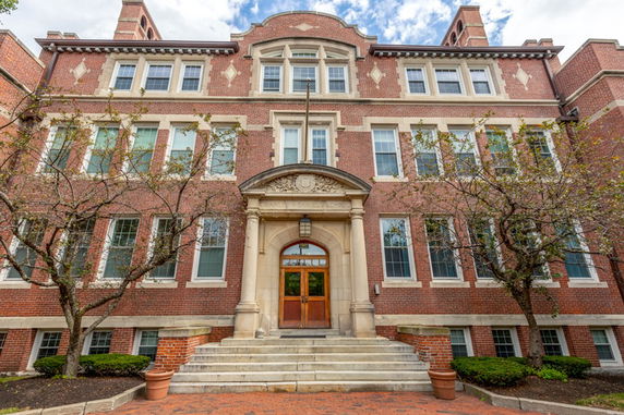 Front view of a multi-story brick building with arched entrance and multiple windows.